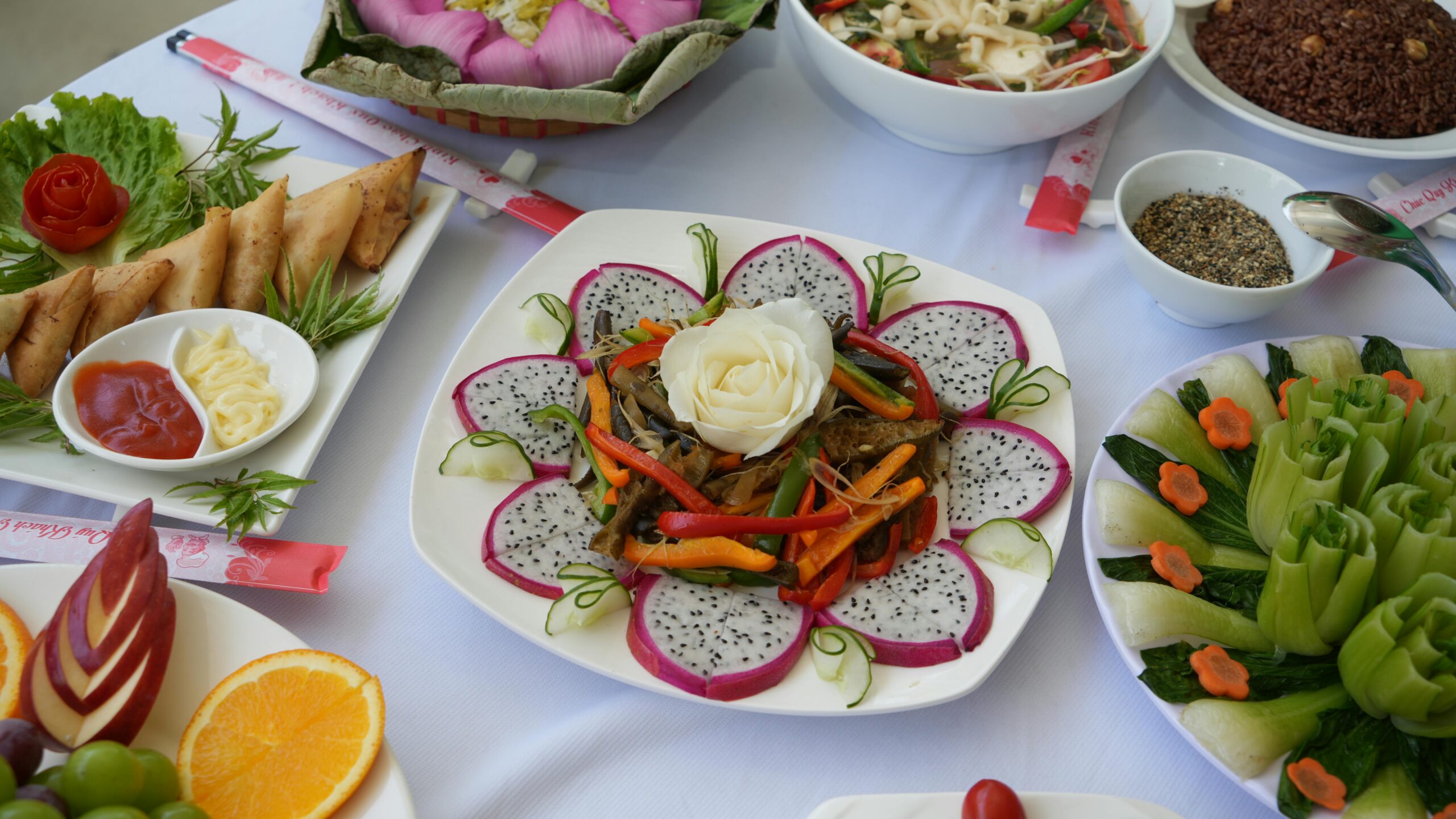 Vibrant display of Asian dishes and fresh fruit platter with dragon fruit, vegetables, and sauces.